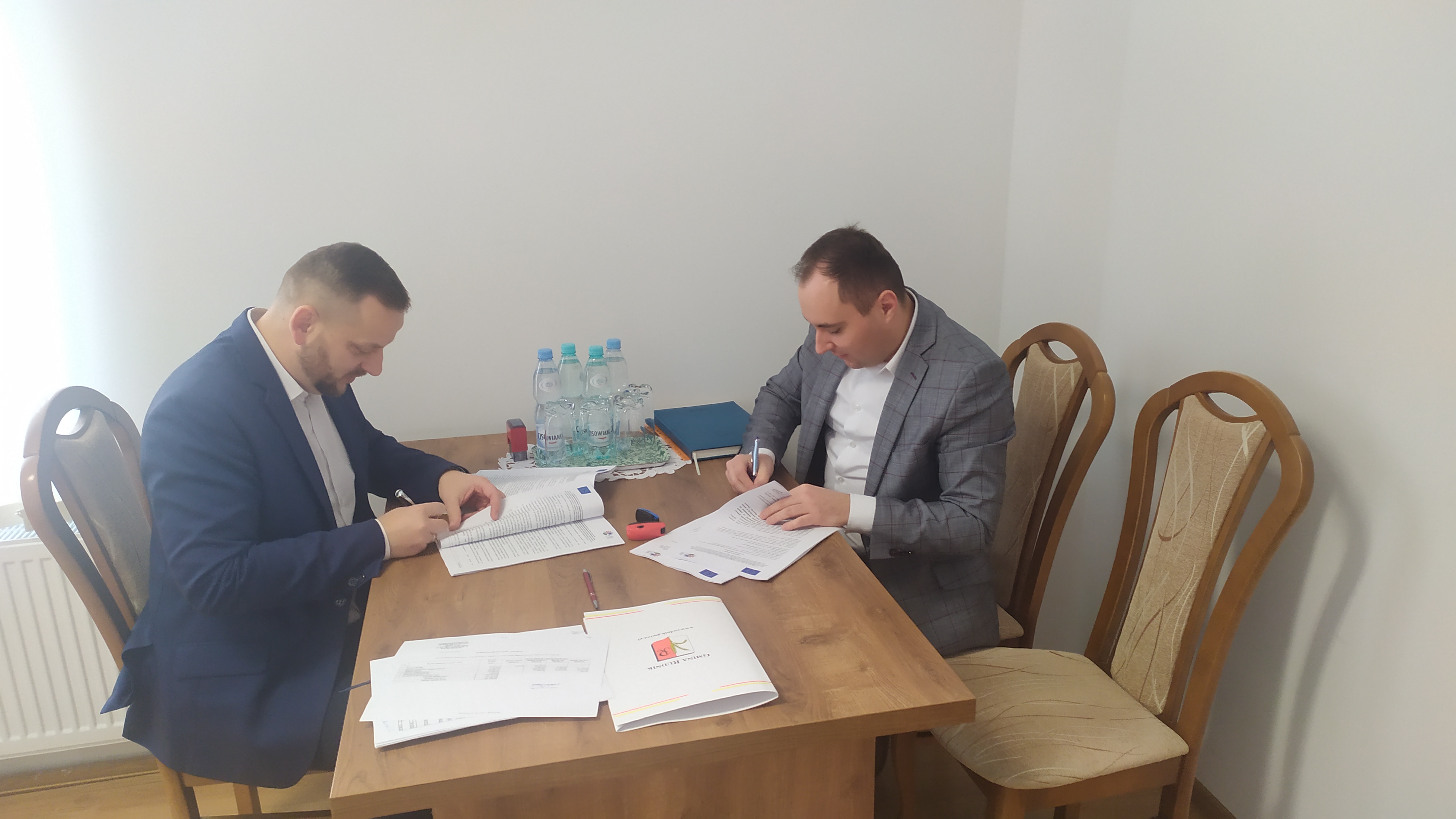 Podpisanie umowy na rozbudowę drogi w Maszowie. Wójt Gminy oraz prezes PRD przy biurku podpisują umowę.